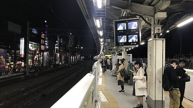 A JR platform at Harajuku at night, a few people waiting under the lights.