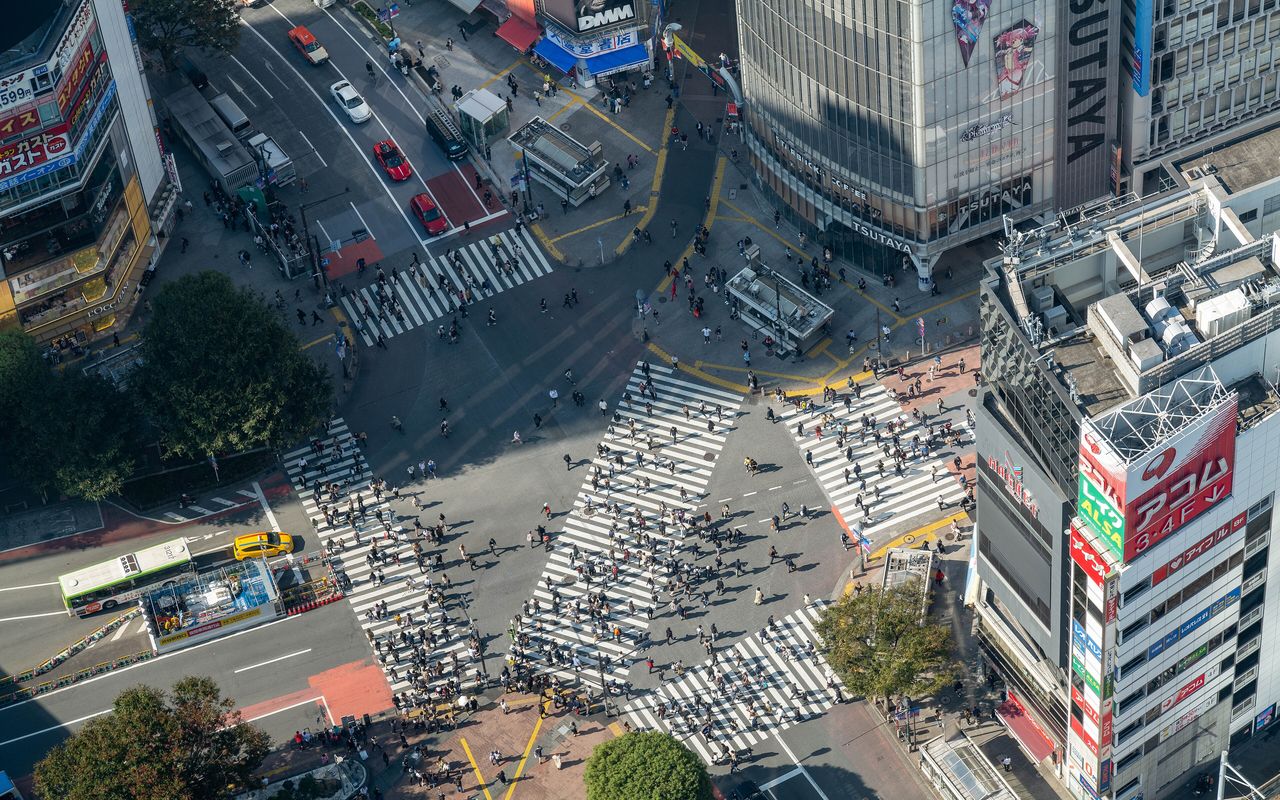 Shibuya crossing from above, the striped crossings full of people.