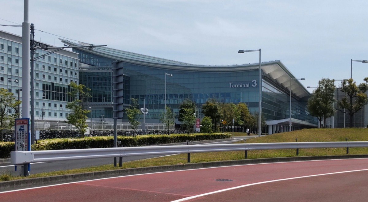 Haneda Airport Terminal 3 from the road, its curved glass front under a grey sky.